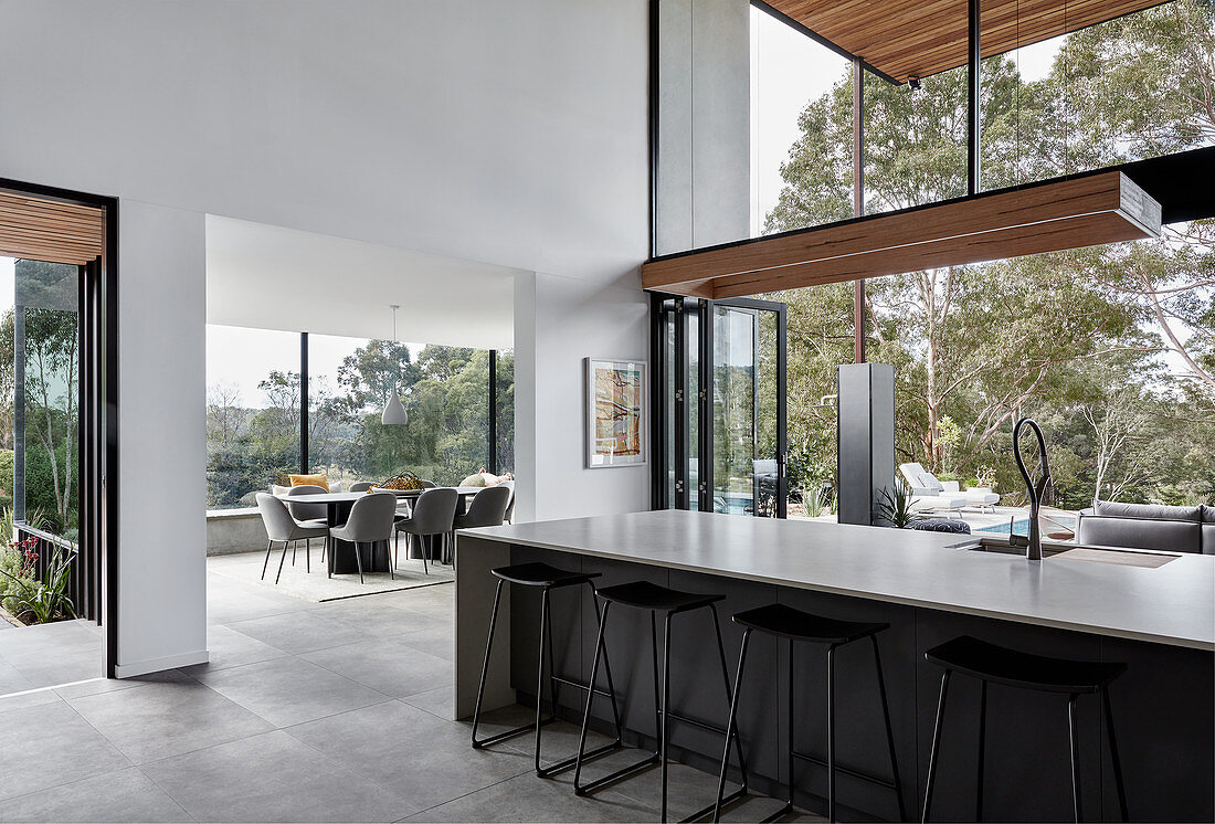 Long kitchen island with bar stools in high-ceilinged interior with glass walls