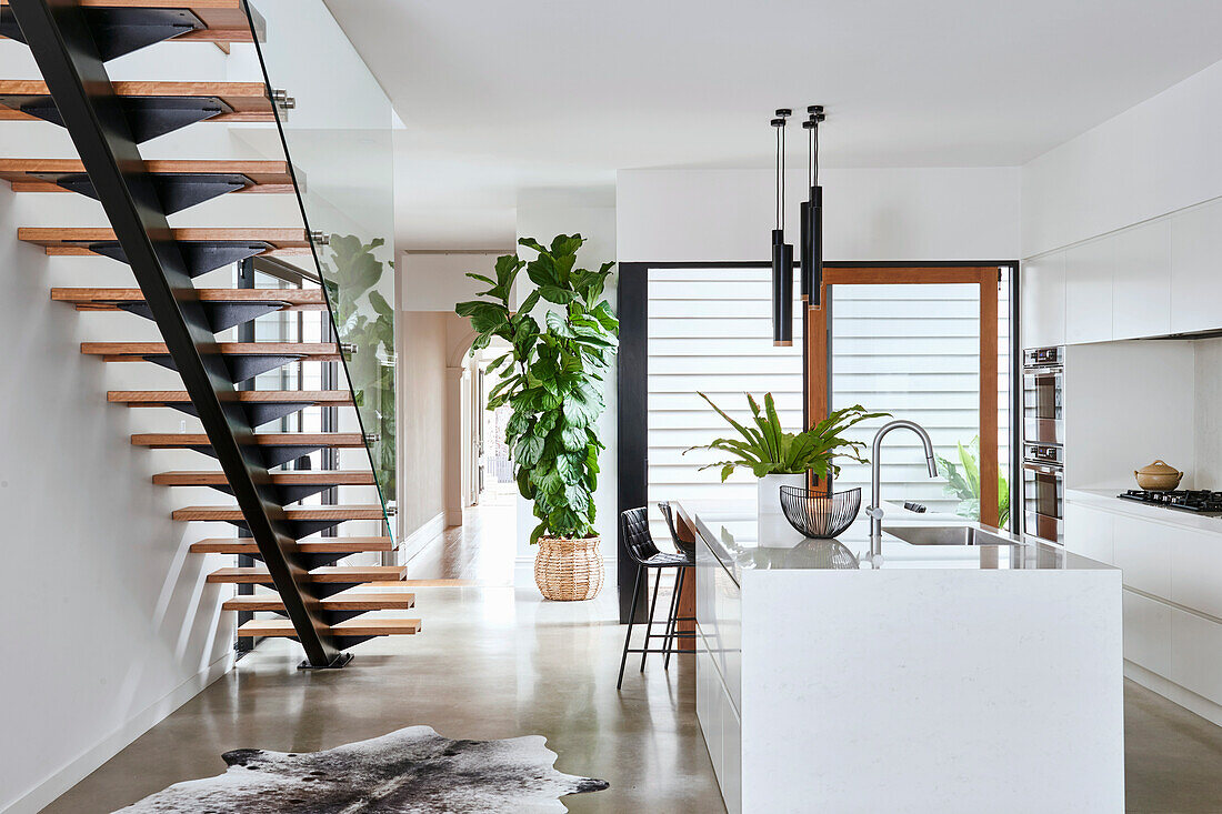 Elegante Weiße Küche mit Kücheninsel und Treppe in offenem Wohnraum