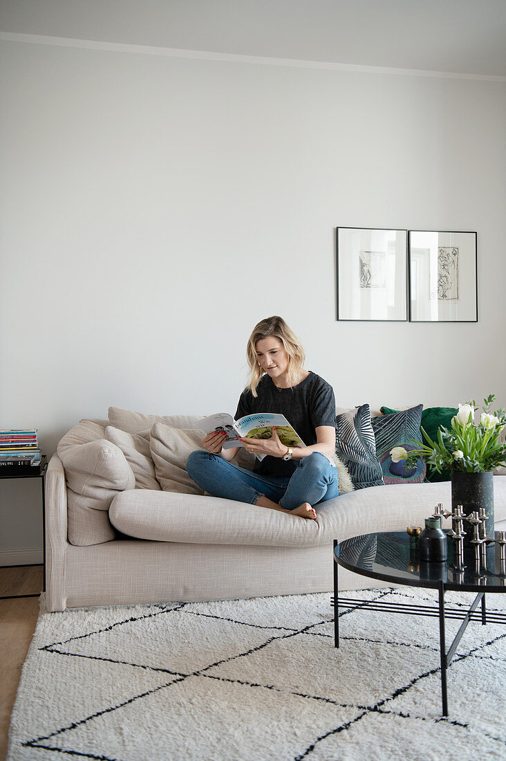 Blonde Frau sitzt mit Zeitschrift auf dem Sofa
