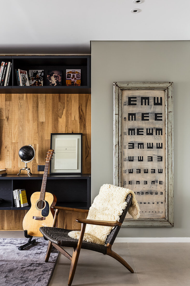 Designerstuhl mit Tierfell, Gitarre vor Wohnzimmerwand und Vintage Sehtafel an der Wand