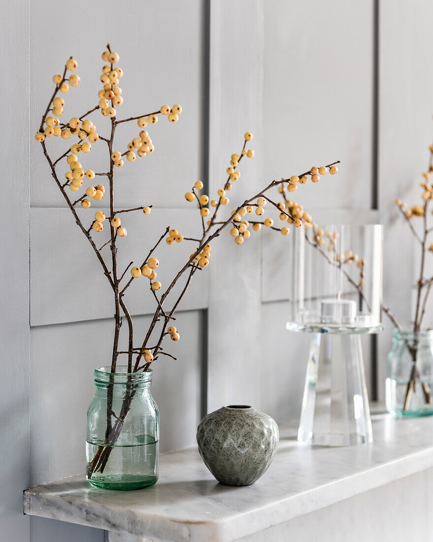 Zweige mit weißen Beeren im Schraubglas als Vase auf dem Sims