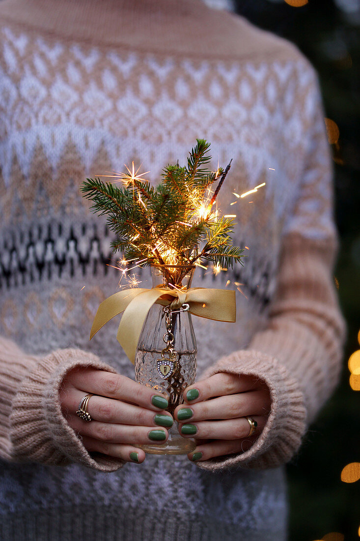 Woman holds posy of spruce branches and sparklers