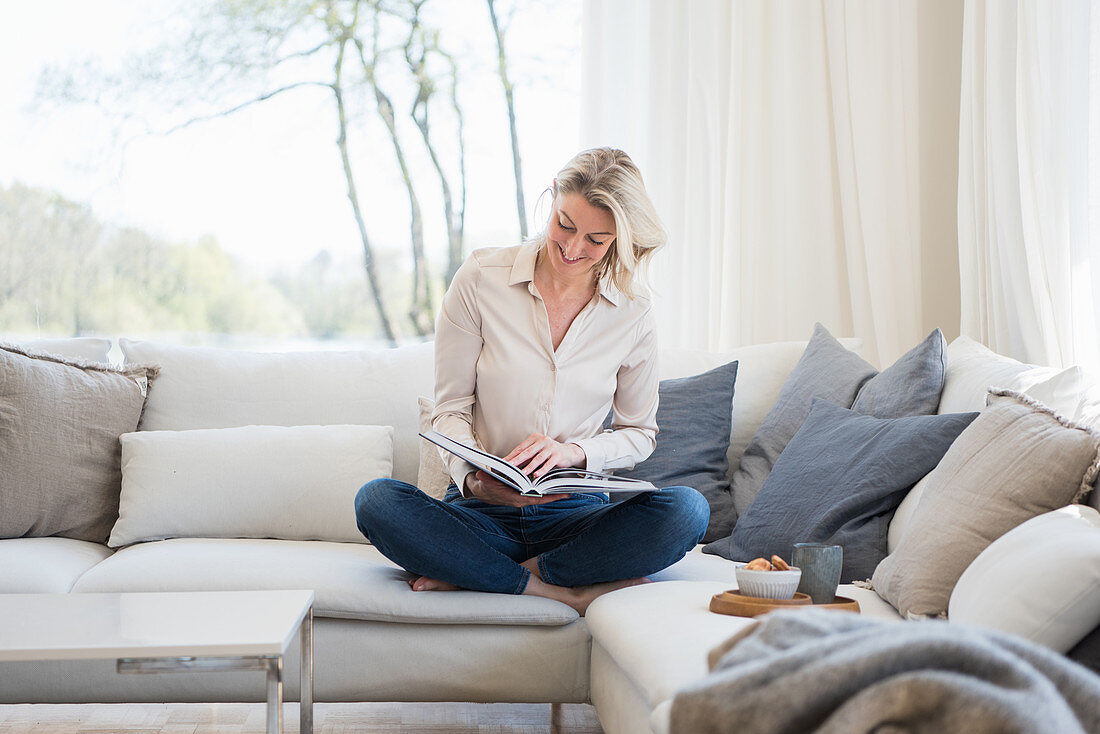Blonde woman reading a book while sitting on comfortable sofa