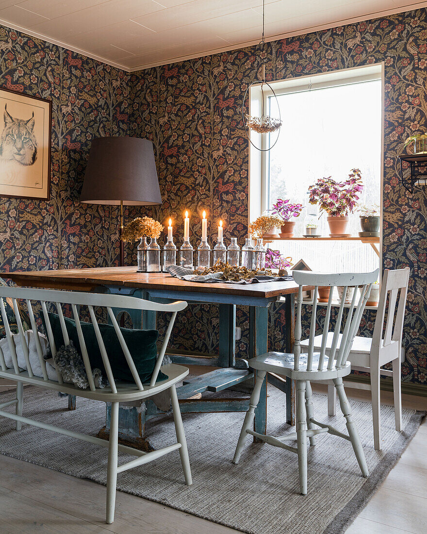 Vintage dining table with candles, chairs and floor lamp in the dining room with wallpaper