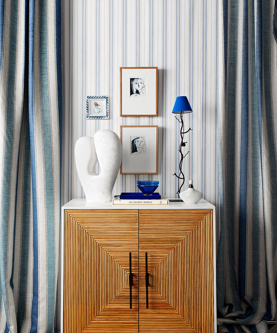 Blue and white ornaments on cabinet flanked by blue and white striped curtains