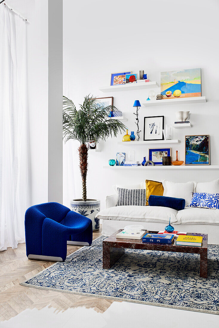 Niedriger Couchtisch, blauer Sessel und weißes Sofa, darüber Regale im Wohnzimmer