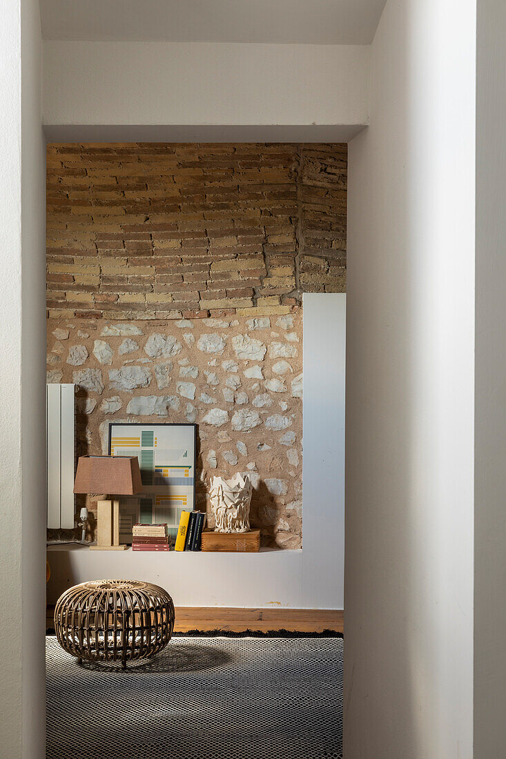Rattan-Pouf und Bücherregal vor Natursteinwand im Wohnzimmer