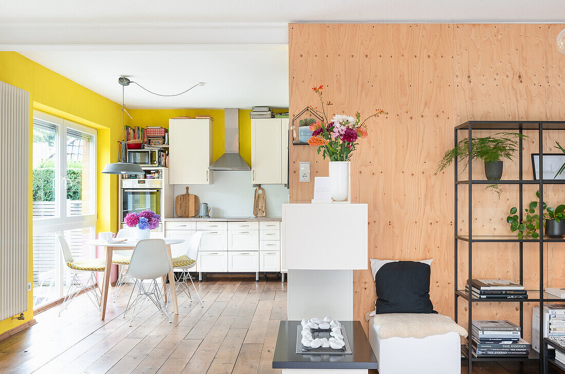 Living area with shelves and wooden room divider, dining area and kitchen in the background