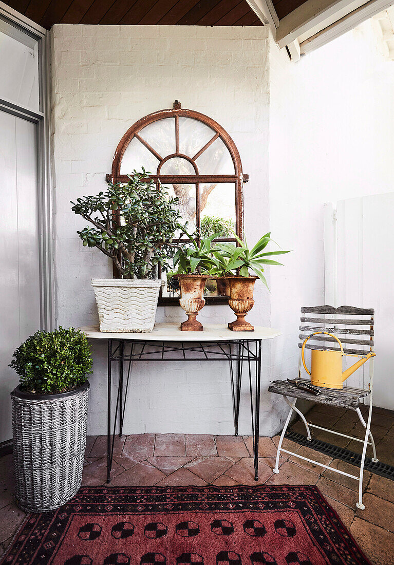 Arched mirror above table with plants on brick floor
