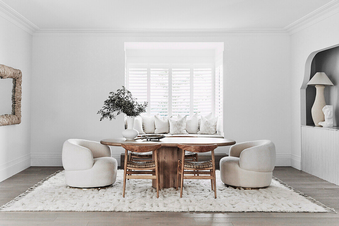 Oval table with chairs and comfortable armchairs in front of window with integrated bench seat