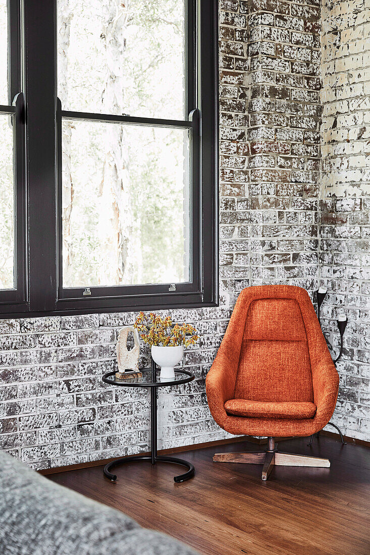 Orangefarbener Sessel und Beistelltisch im Zimmer mit Backsteinwänden