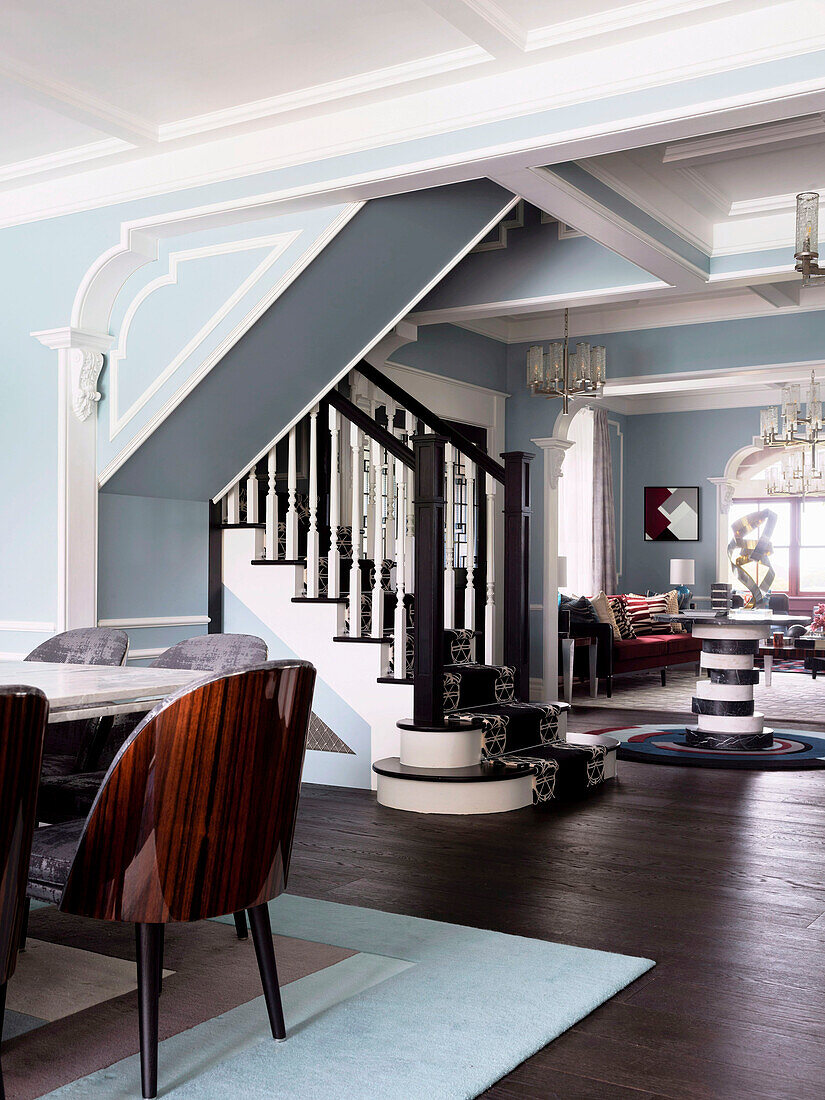 Esstisch mit Designerstühlen in offenem Wohnraum mit hellblauer Wand, im Hintergrund Treppenaufgang