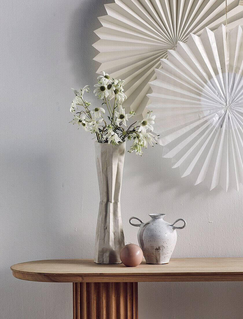 DIY-Papierschneeflocken an der Wand, davor Vase mit Blumen auf Konsolentisch
