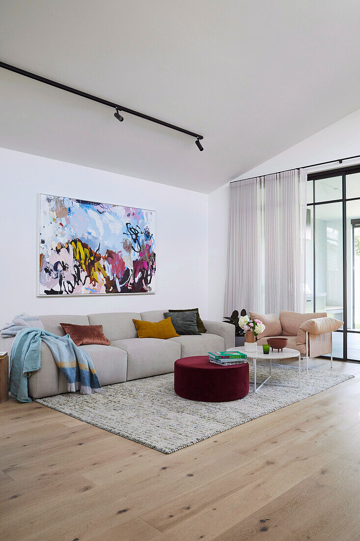 Sofa mit Kissen, darüber Kunstwerk, Sessel, Couchtisch aus Marmor und Ottomane mit Samtbezug im Wohnzimmer
