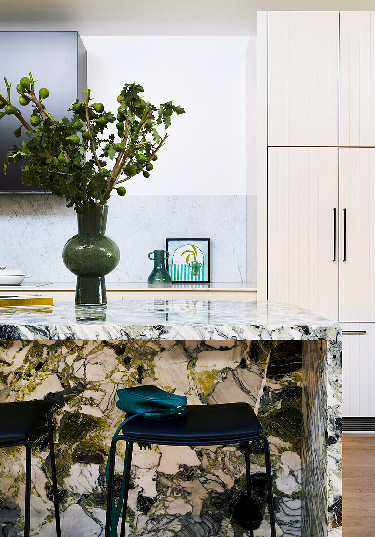 Kitchen island with green marble worktop, bar stools and vase with green branches