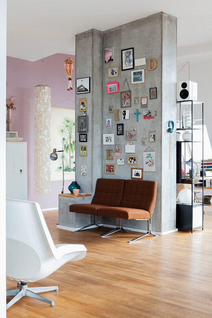 Betonwand als Raumteiler mit Bildern, Fotos und Dekobuchstaben, darunter braune Sessel in offenem Wohnraum