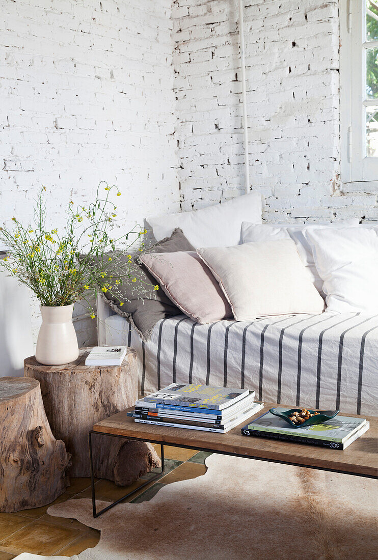 Sofa mit Kissen, Couchtisch und Baumstamm-Hocker im Zimmer mit weiß getünchter Ziegelwand