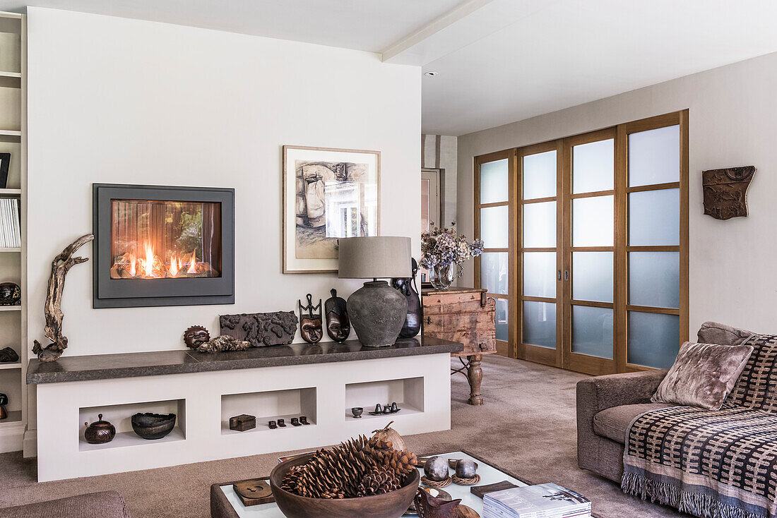 Opaque sliding doors in living room with Indian wool carpet. A Dru gas fire has been set into the wall above a display area featuring wooden African masks