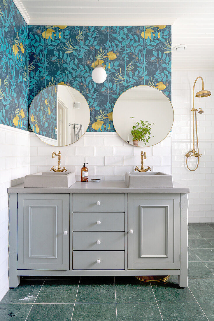 Washstand with two countertop basins below round mirrors on blue patterned wall in bathroom