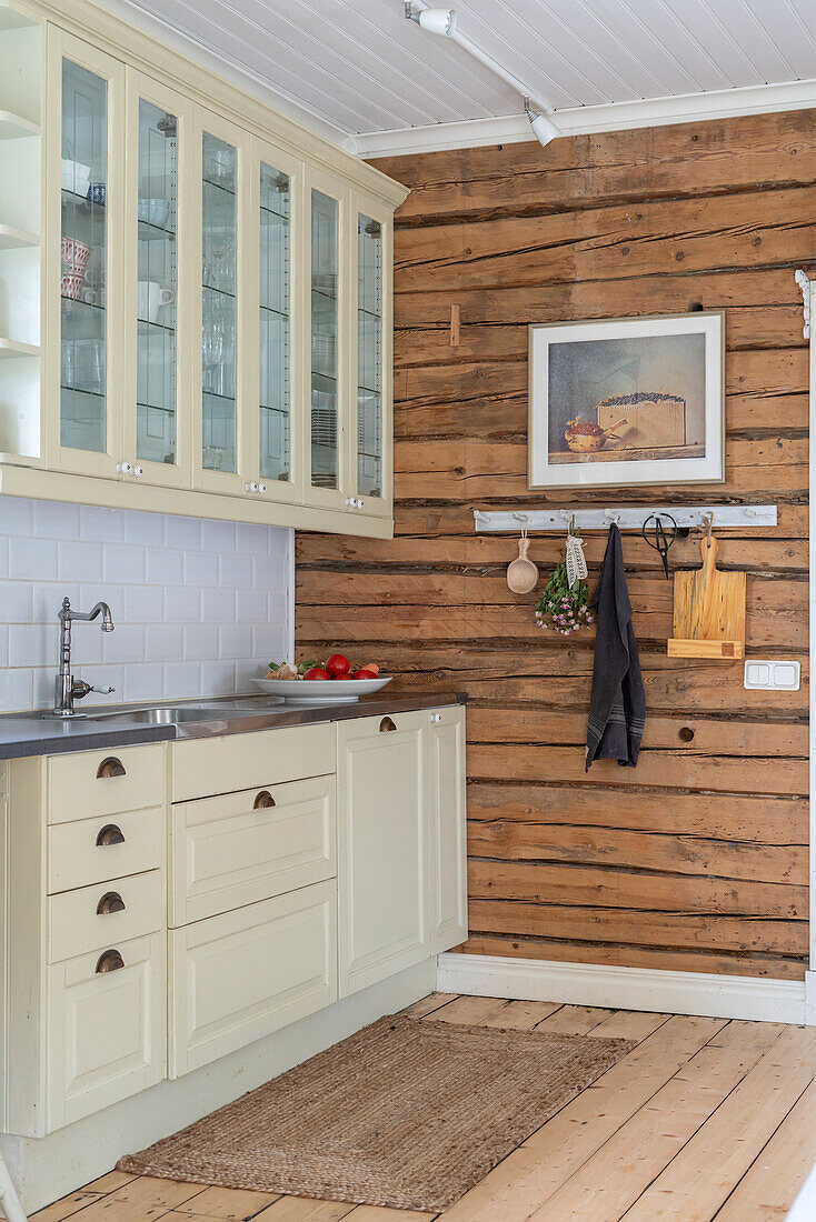 Cremefarbene Küchenzeile mit Glas-Oberschrank und raue Holzwand in der Küche