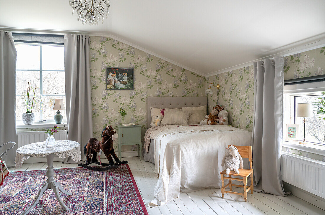 Bed, high chair and rocking horse in room with floral wallpaper