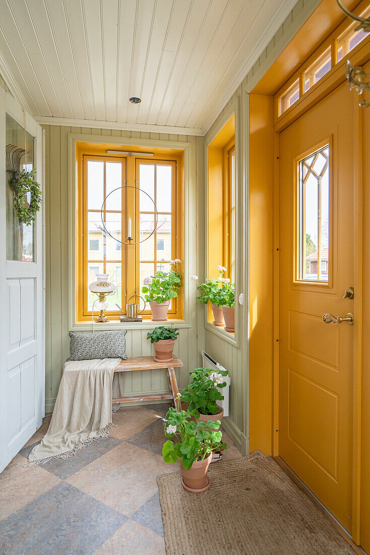Potted geraniums in hallway with yellow front door and wooden panelling