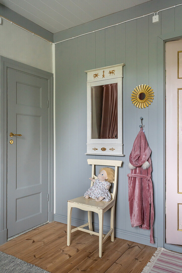 Alter Holzstuhl, darüber Spiegel im Kinderzimmer mit hellgrau gestrichener Holzverkleidung