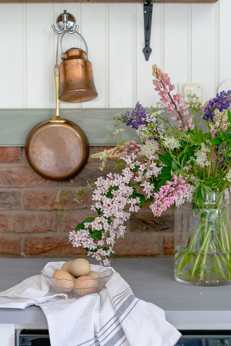 Frische Eier und sommerlicher Blumenstrauß auf Küchenarbeitsplatte, Kupfertöpfe an der Wand