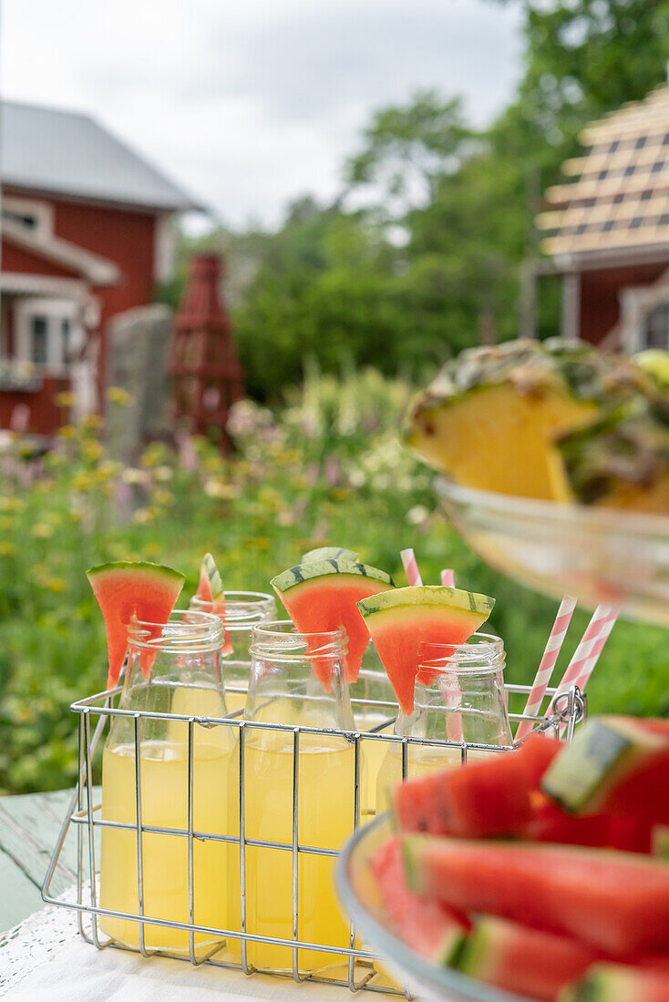 Flaschen mit kaltem Saft und Melone im Flaschenhalter auf Gartentisch