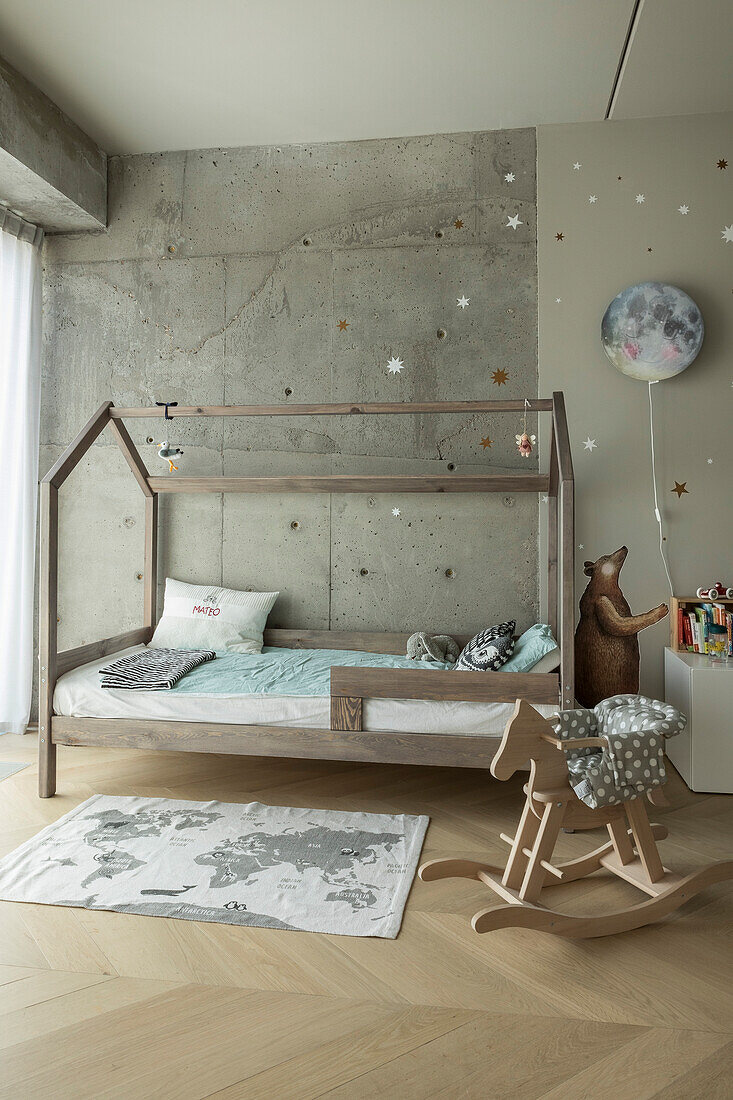 House-shaped child's bed against concrete wall and rocking horse in foreground