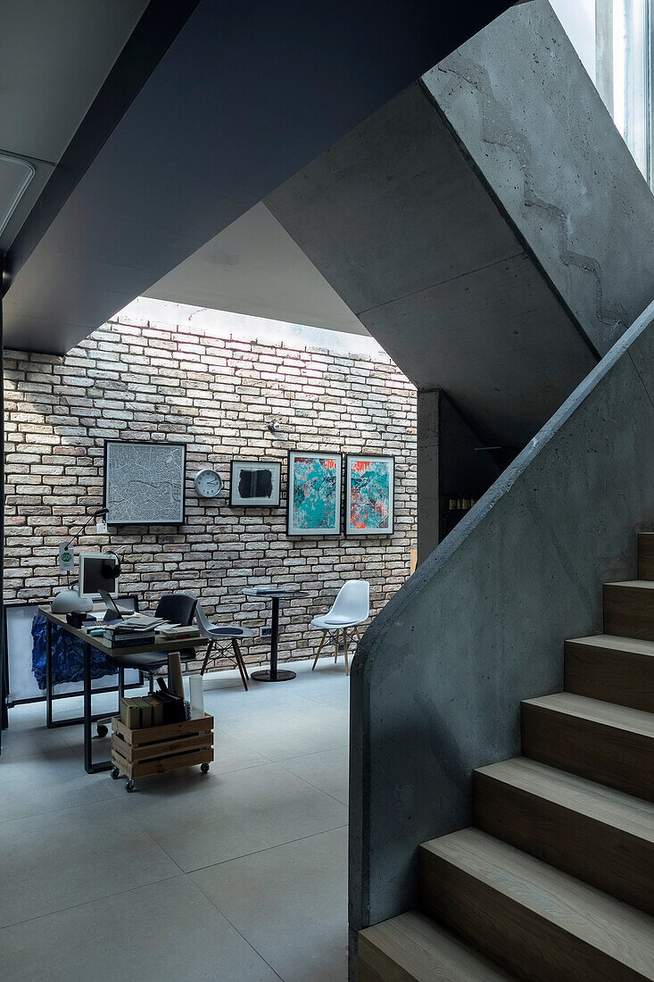 Home Office vor Ziegelwand in einer Loft-Wohnung, Treppenaufgang im Vordergrund