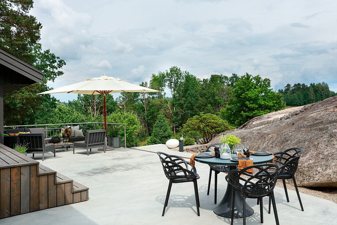 Modern outdoor lounge with grey upholstered furniture and dining area on the roof terrace surrounded by boulders