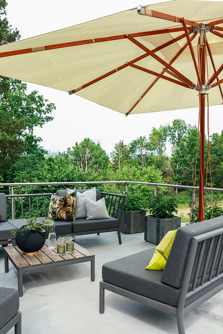 Modern outdoor lounge with grey upholstered furniture under a parasol on roof terrace