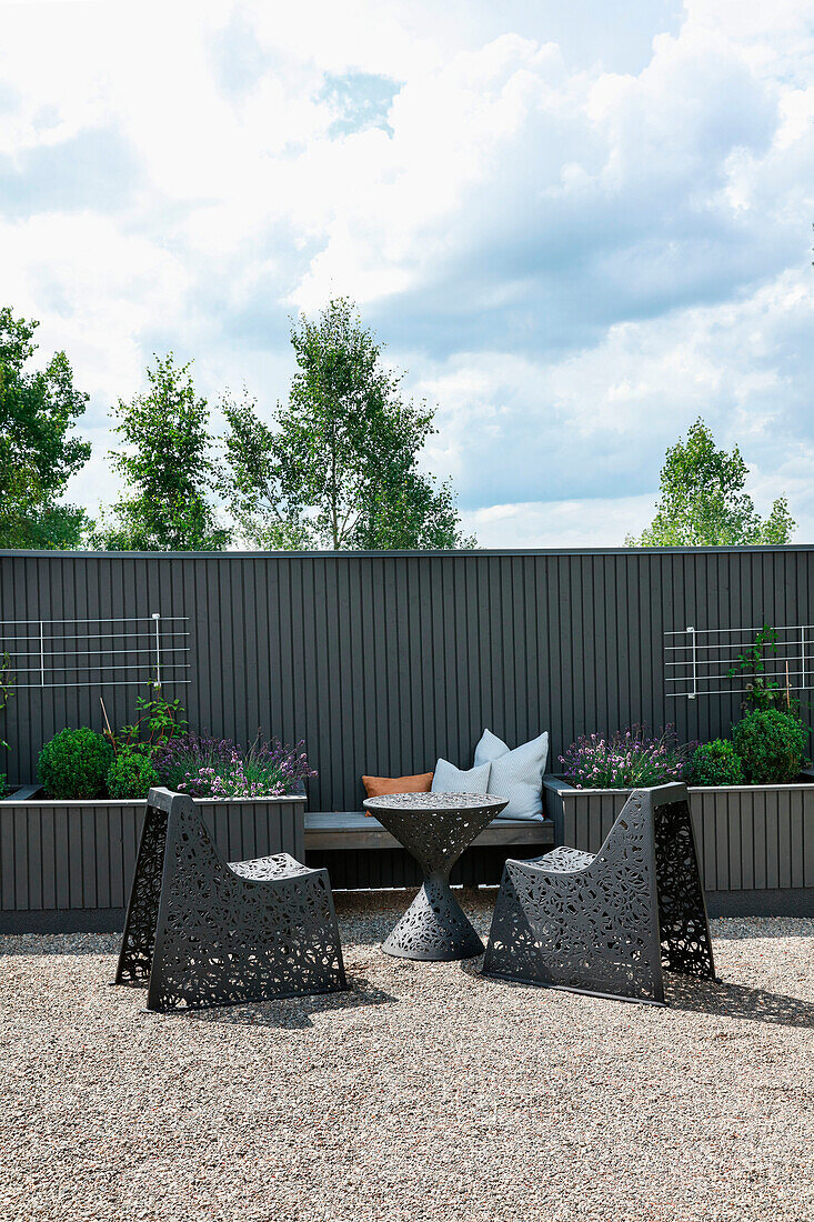 Moderne Gartenstühle vor Bank zwischen zwei Hochbeeten an Sichtschutzwand in Grau