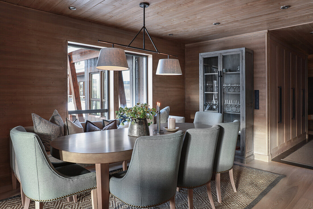 Ovaler Esstisch mit grauen Polsterstühlen in elegantem Esszimmer mit Holzverkleidung