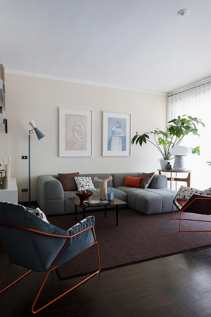 Graue Sofagarnitur und Sessel mit Metallstruktur im Wohnzimmer mit dunklem Boden