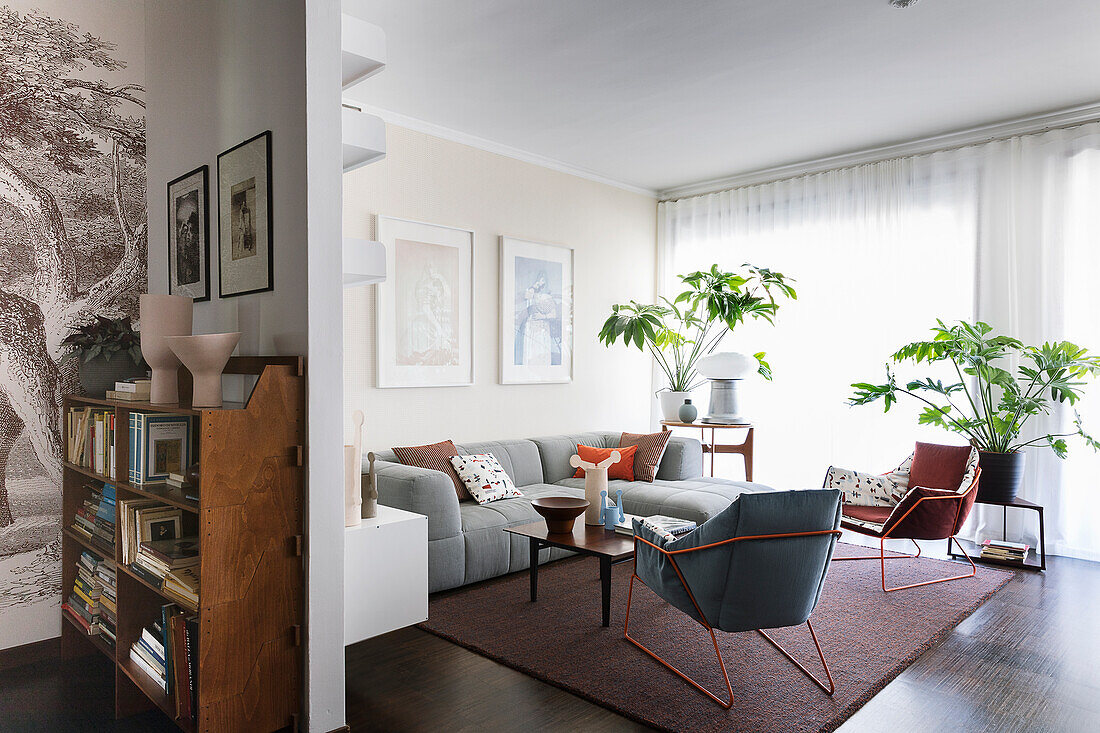 Graue Sofagarnitur, Zimmerpflanzen und Sessel mit Metallstruktur im Wohnzimmer mit dunklem Boden