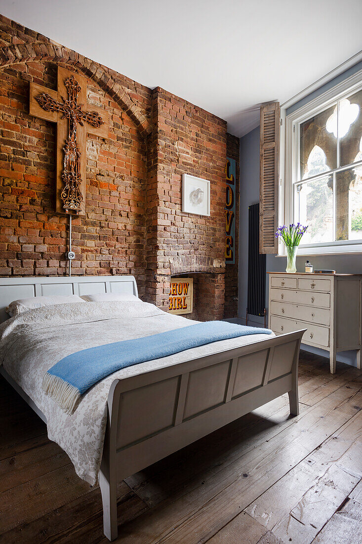 Guest bedroom with double bed below cross on brick wall