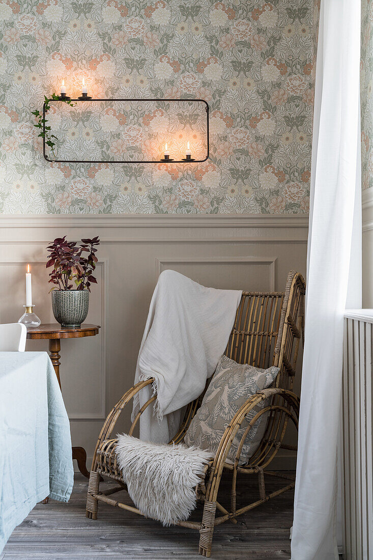 Rustic rattan armchair below modern candle sconce on wall with vintage-style wallpaper