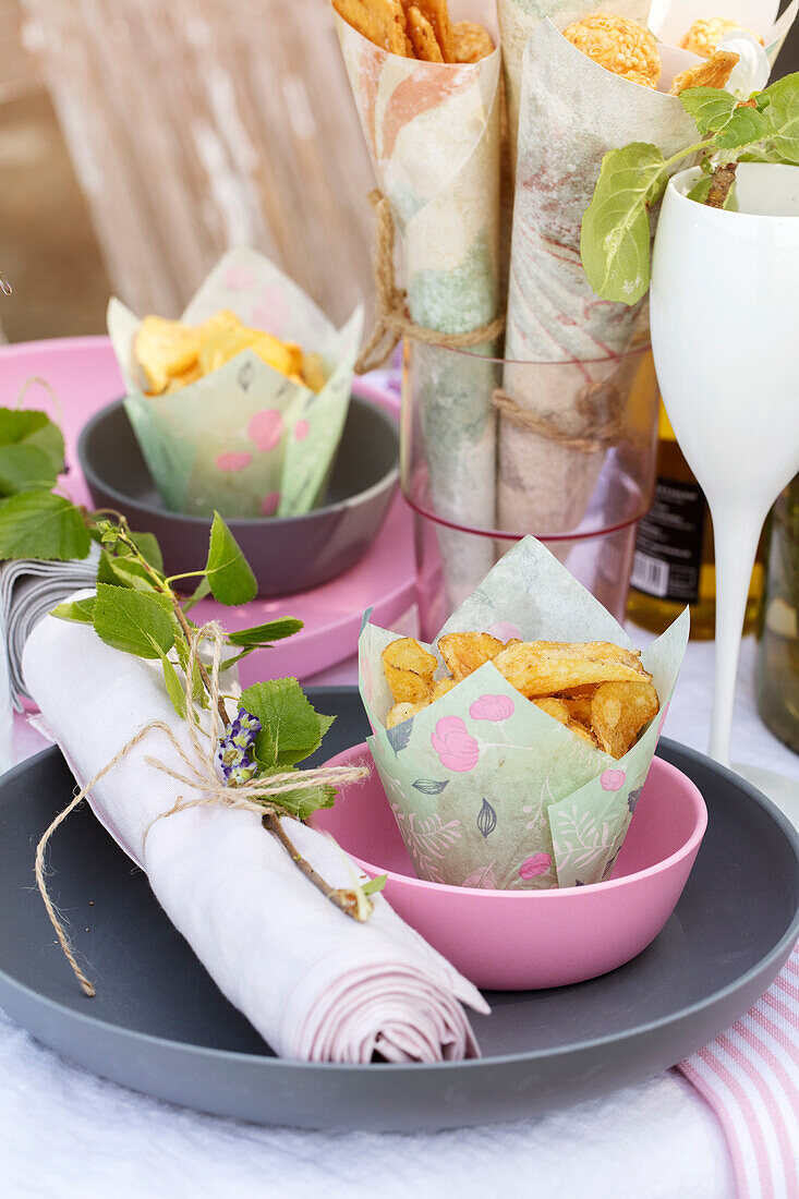 Linen napkin decorated with twig and small bowls of homemade crisps on a festive table