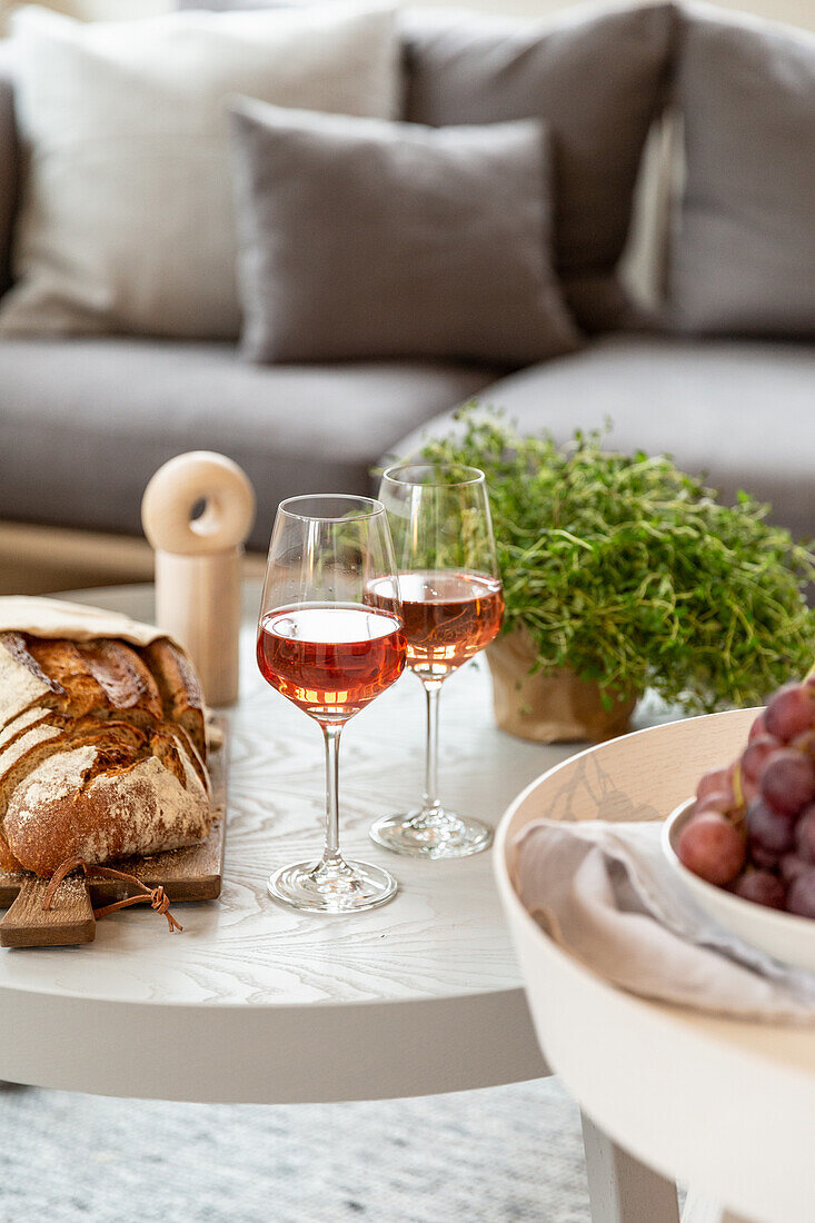 Two glasses of wine, bread and grapes on coffee table in front of sofa