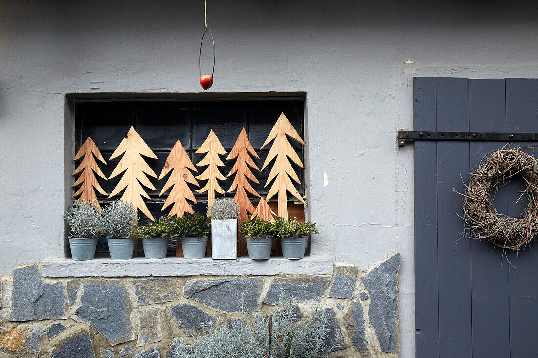 Wooden fir trees and plants on windowsill with wreath on house wall