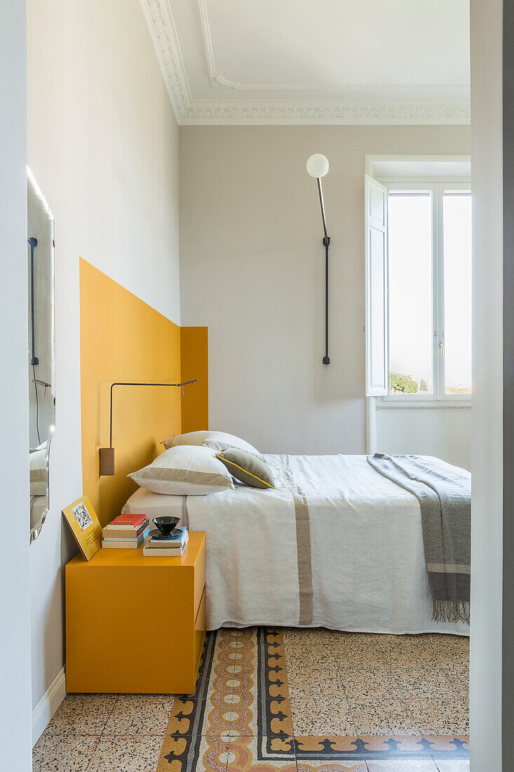 Doppelbett vor gelber Wand, daneben farblich passender Nachtisch