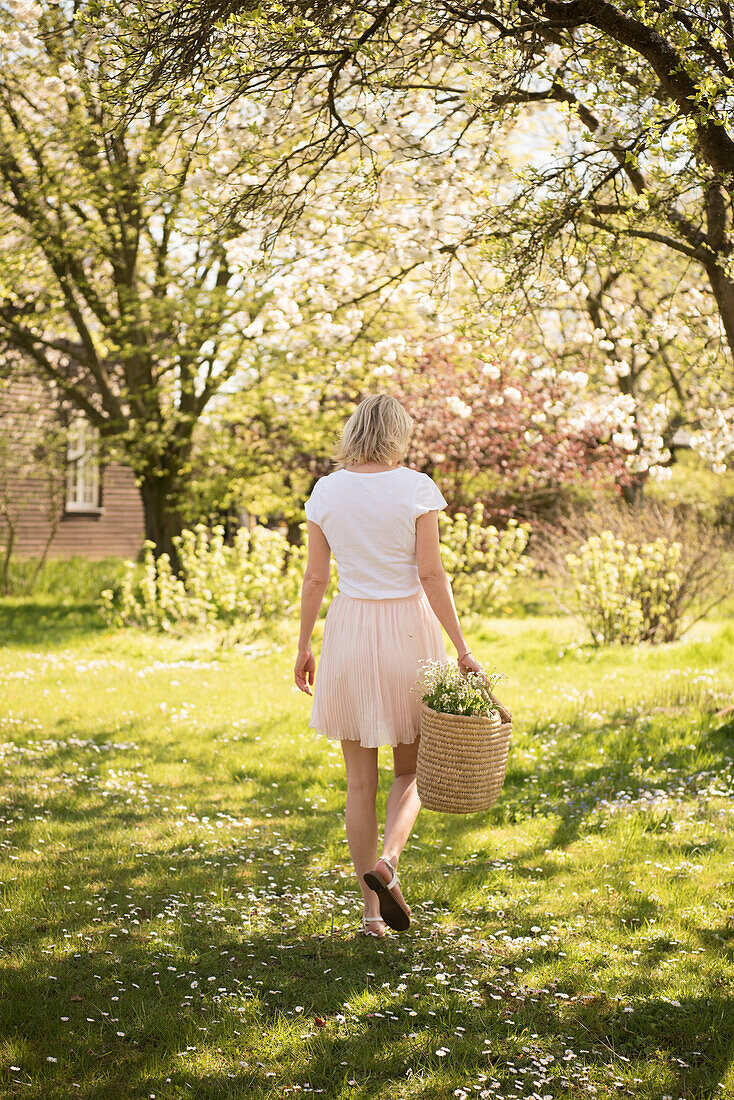 Blond woman in white t-shirt and skirt with flower basket in the spring garden