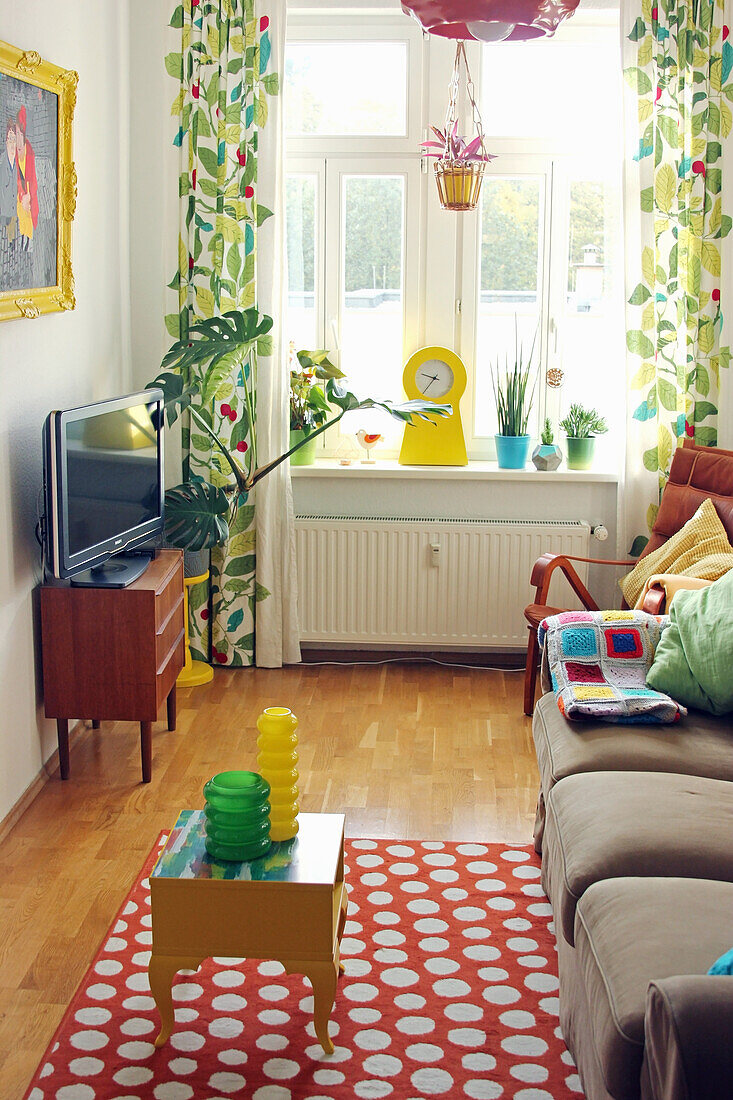 Wohnzimmer mit Sofa, gepunktetem Teppich, Fernseher und bunten Vorhängen