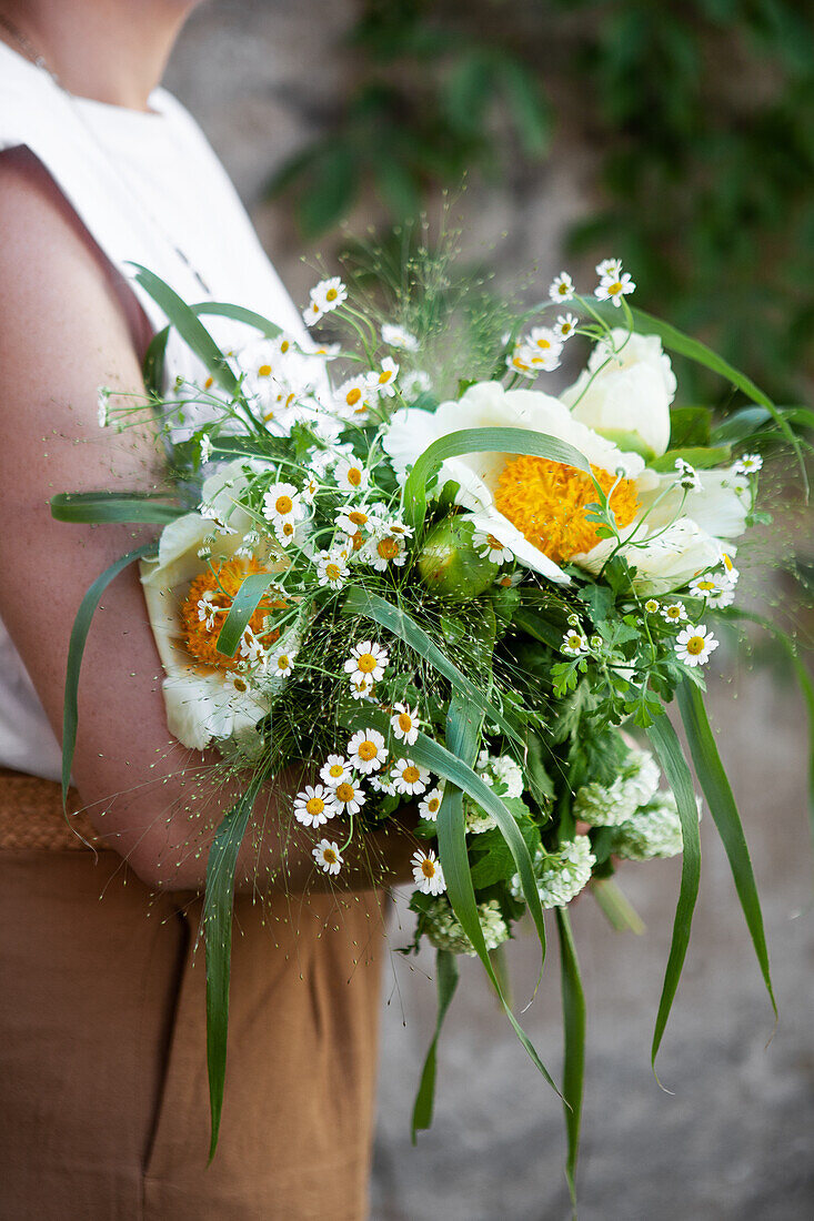 Woman holding white bouquet of peonies, viburnum, feverfew and grasses
