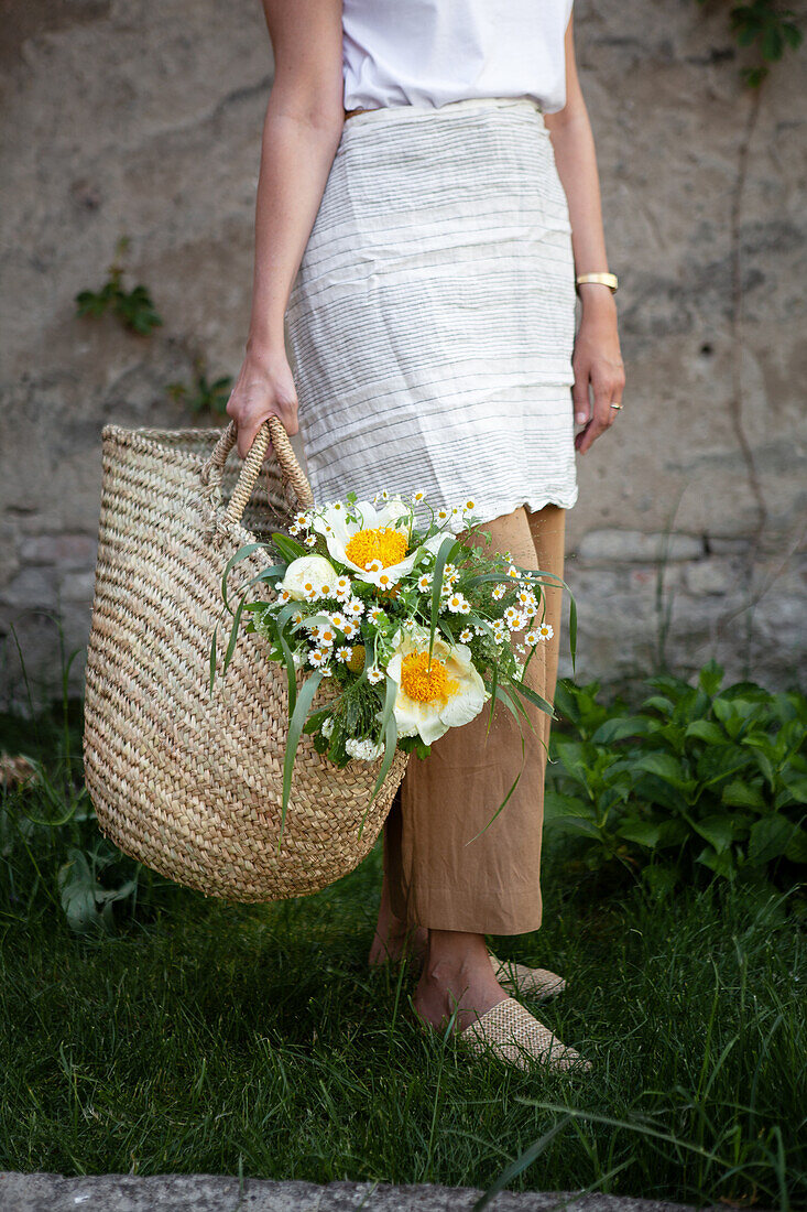 Woman carrying basket bag with white bouquet of peonies, snowball, motherwort and grasses