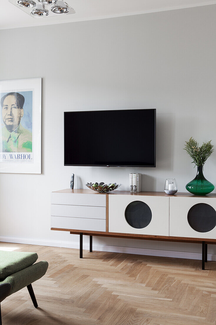 Sideboard below wall-mounted TV in living room with herringbone parquet floor