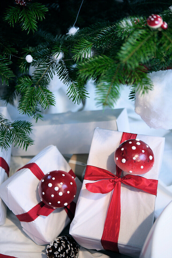 Weihnachtsgeschenke mit roten Schleifen und Fliegenpilzen unter geschmücktem Tannenbaum