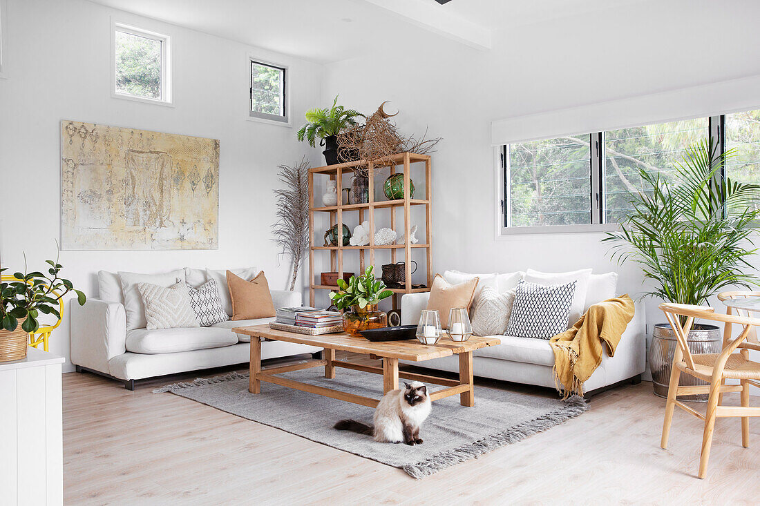 White sofas with throw pillows, shelving unit, and wooden coffee table in a bright living room